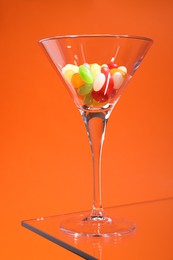 Photo of Martini glass with many tasty colorful candies on table against orange background