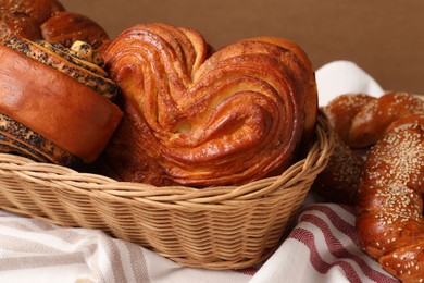 Wicker basket and different tasty freshly baked pastries on tablecloth, closeup