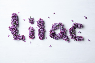 Photo of Word LILAC made with beautiful purple flowers on white wooden background, flat lay