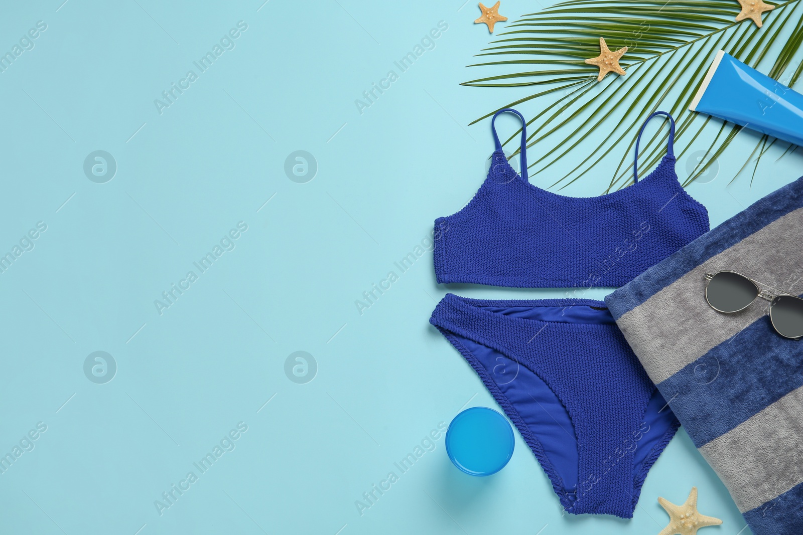 Photo of Beach towel, swimsuit, sunglasses sun and protection product on light blue background, flat lay. Space for text