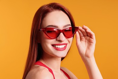 Photo of Happy woman with red dyed hair and sunglasses on orange background