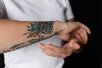 Photo of Woman applying cream on her arm with tattoos against black background, closeup