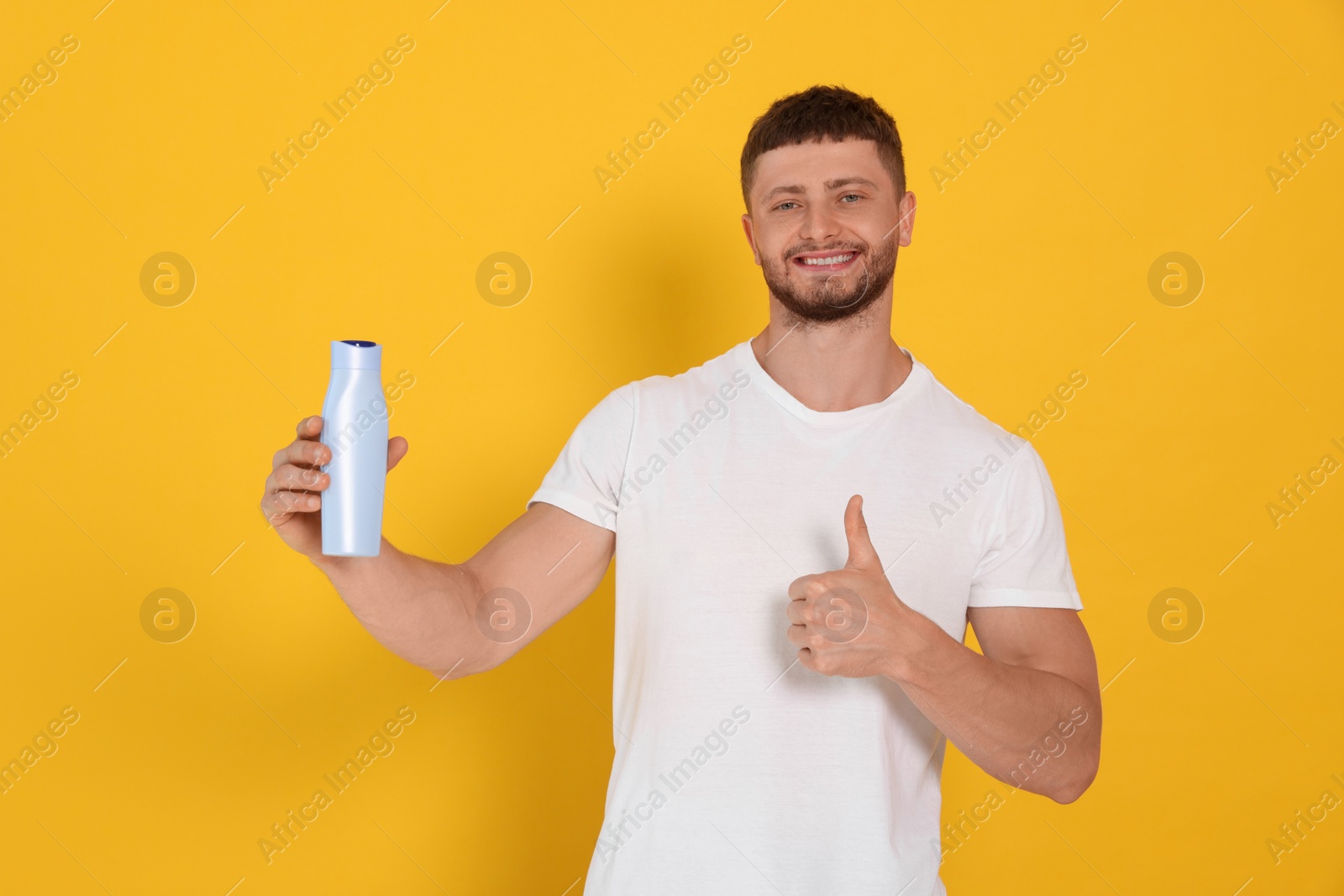 Photo of Handsome young man holding bottle of shampoo on orange background