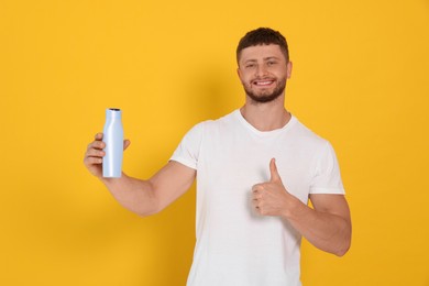 Handsome young man holding bottle of shampoo on orange background