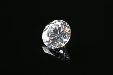 Photo of Beautiful shiny diamond on black mirror surface
