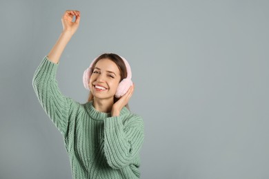 Photo of Happy woman wearing warm earmuffs on grey background, space for text