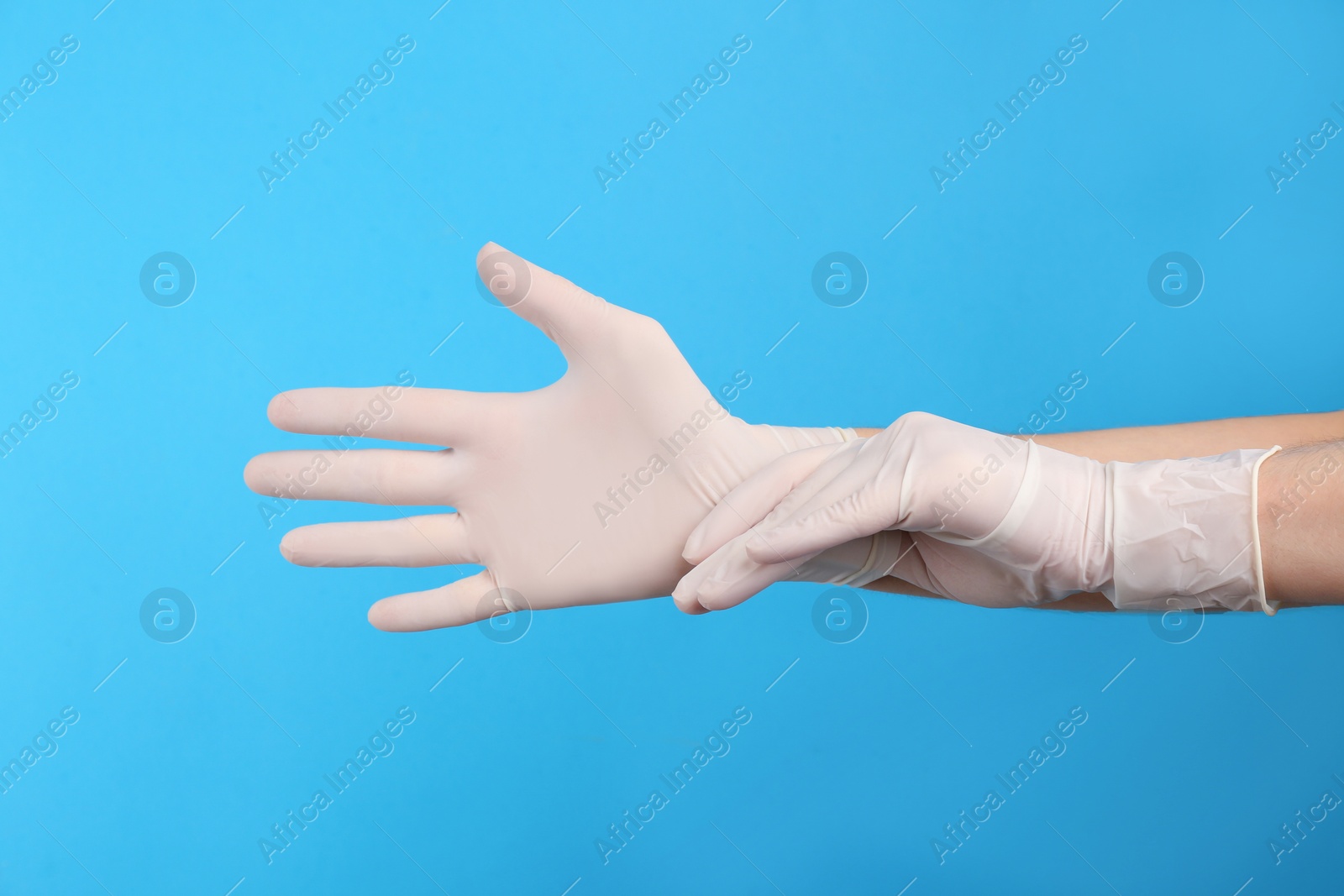 Photo of Person putting on medical gloves against light blue background, closeup of hands