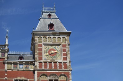 Beautiful building of central railway station with clock against blue sky, low angle view. Space for text