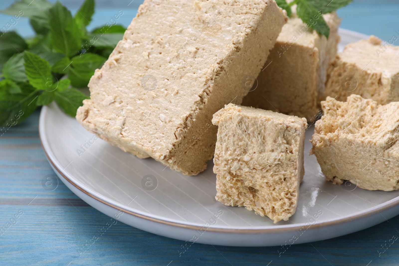 Photo of Pieces of tasty halva and mint on light blue wooden table, closeup