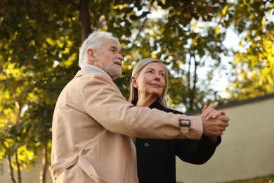 Photo of Affectionate senior couple dancing together outdoors, low angle view