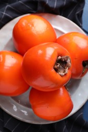 Delicious ripe persimmons and plate on table, top view