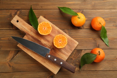 Photo of Fresh ripe tangerines with green leaves on wooden table, flat lay
