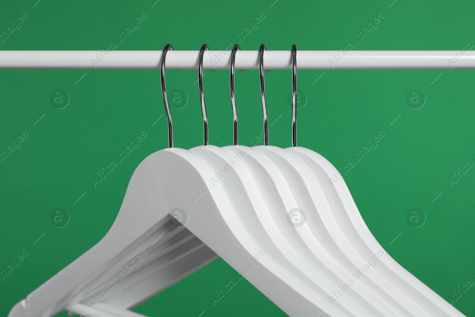 Photo of Empty clothes hangers on rack against green background, closeup