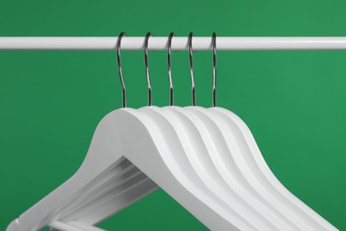 Photo of Empty clothes hangers on rack against green background, closeup