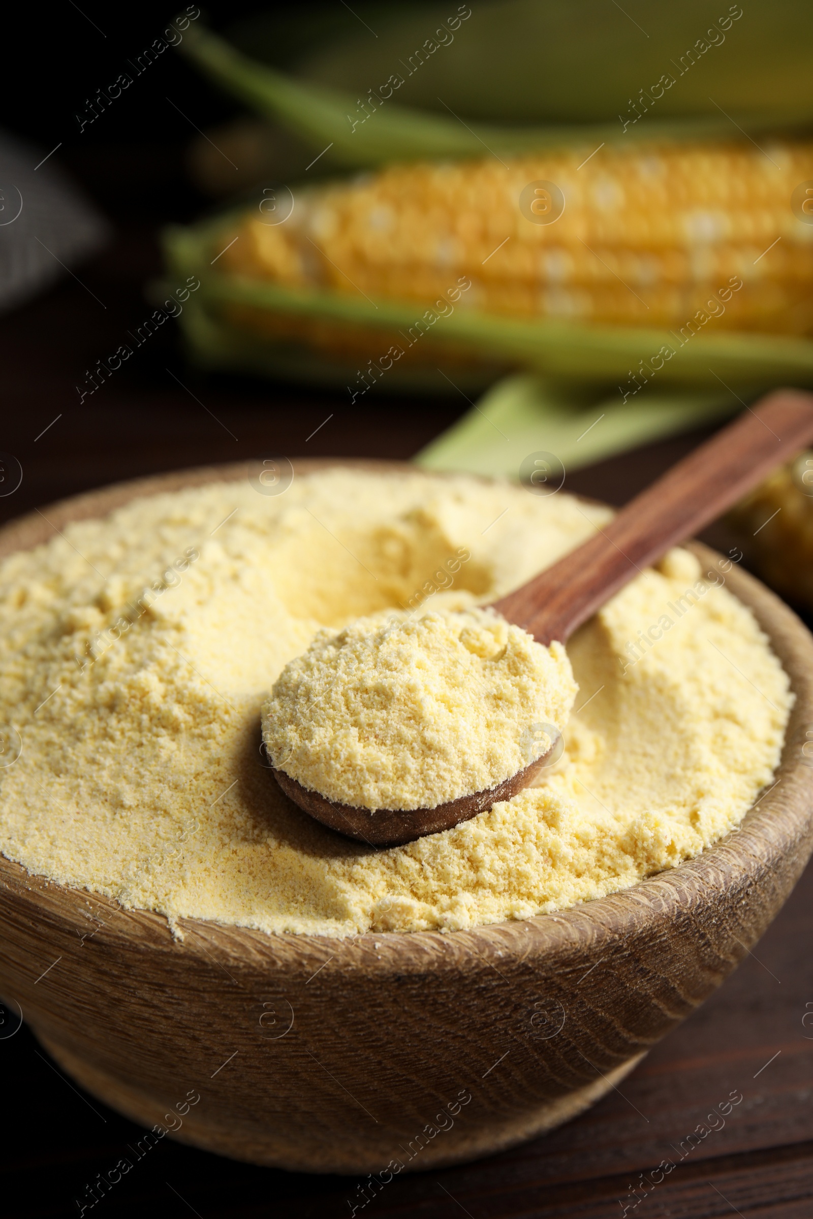 Photo of Corn flour in bowl and fresh cobs on wooden table