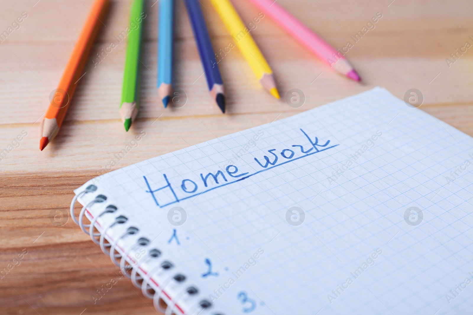 Photo of Word HOMEWORK in notebook and pencils on wooden table, closeup