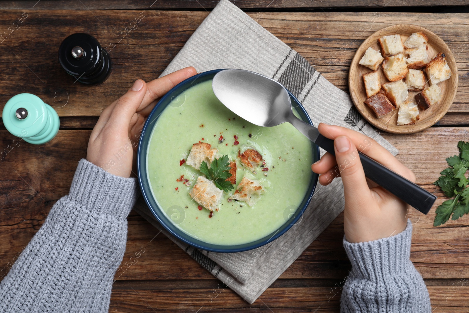 Photo of Woman eating delicious asparagus soup at wooden table, top view