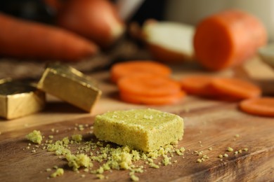 Photo of Bouillon cube and cut carrot on wooden board, closeup