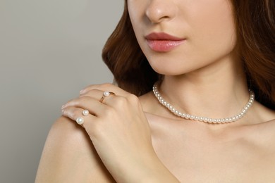 Young woman wearing elegant pearl jewelry on grey background, closeup