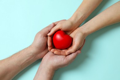 Photo of Couple holding red decorative heart on light blue background, top view