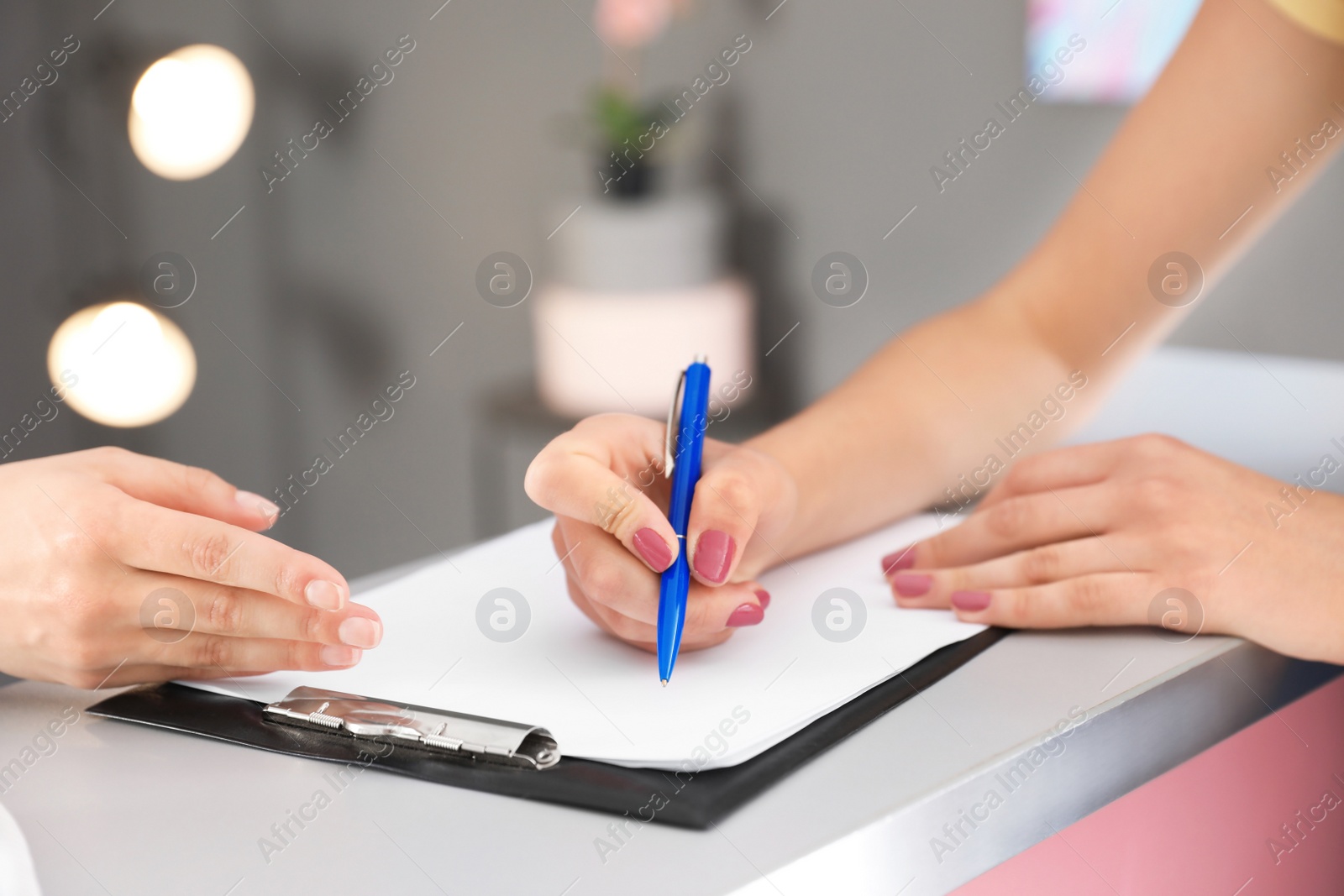 Photo of Young woman filling application form at reception desk
