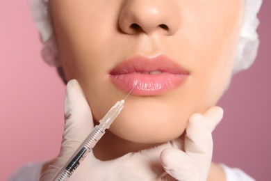 Young woman getting lip injection on color background, closeup