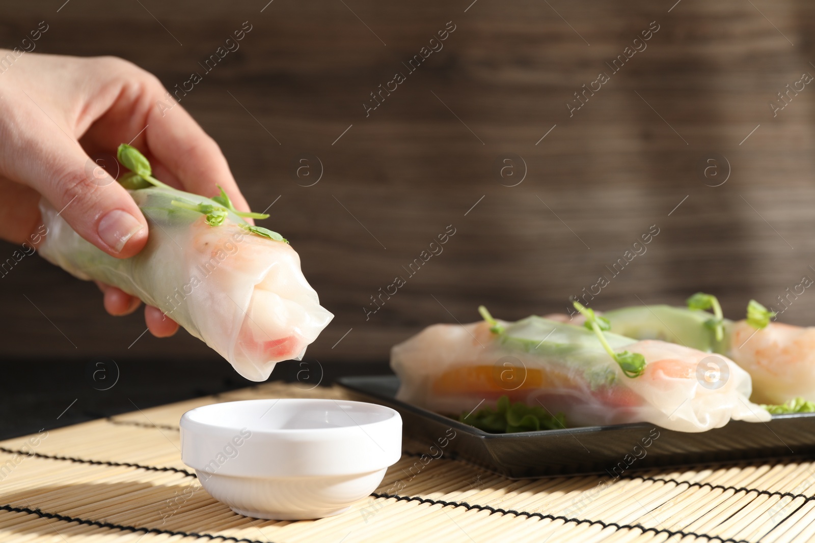 Photo of Woman dipping delicious spring roll into sauce at table, closeup