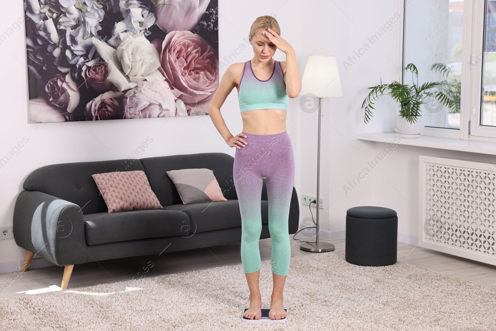 Photo of Worried woman standing on floor scale at home