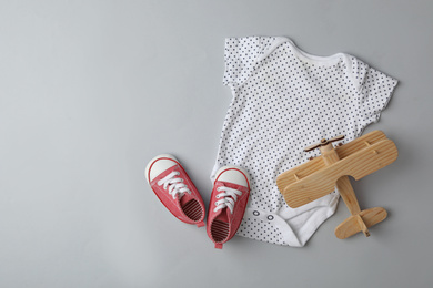 Photo of Child's shoes, bodysuit and wooden airplane on grey background, flat lay with space for text
