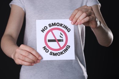 Woman holding card with no smoking sign on black background, closeup