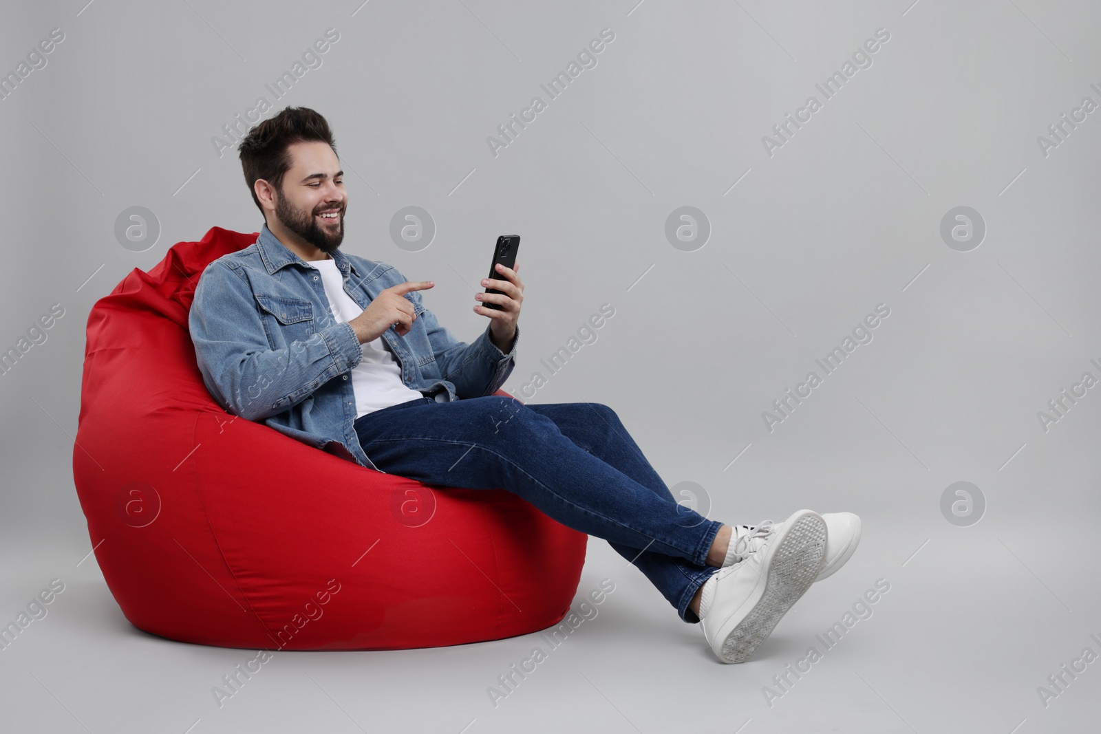 Photo of Happy young man using smartphone on bean bag chair against grey background