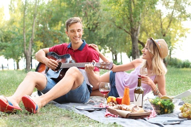 Photo of Young man playing guitar to his girlfriend in park. Summer picnic