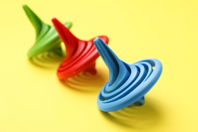 Photo of Many colorful spinning tops on yellow background, closeup
