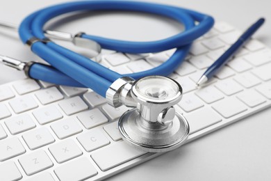 Keyboard and stethoscope on white background, closeup