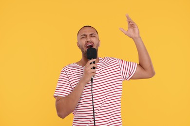 Handsome man with microphone singing on orange background