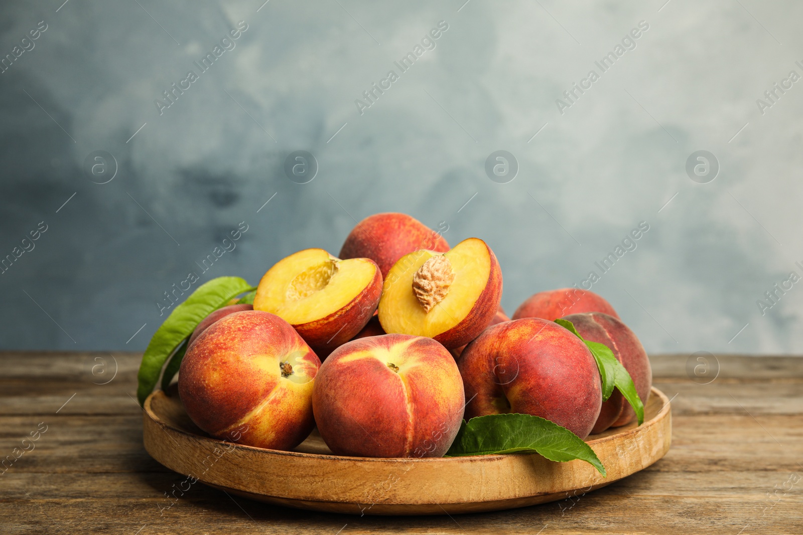 Photo of Plate with fresh peaches and leaves on wooden table against blue background