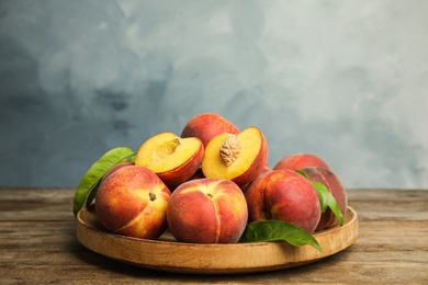 Plate with fresh peaches and leaves on wooden table against blue background