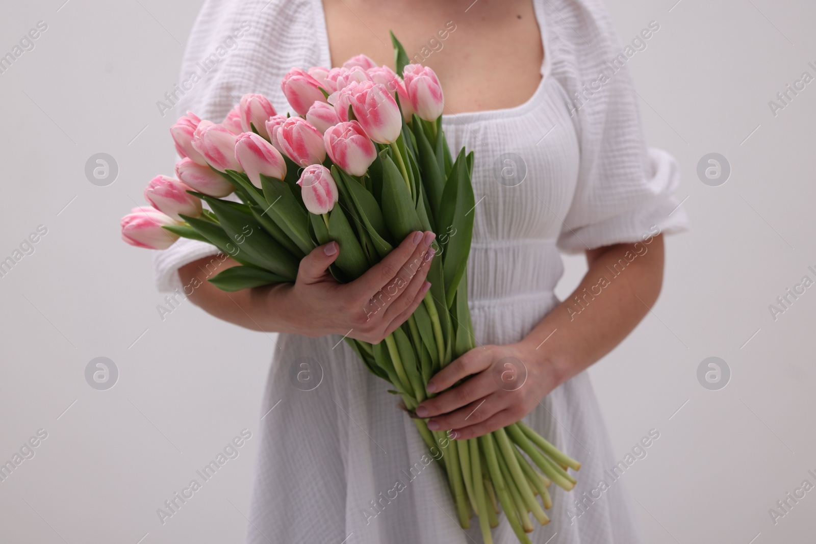 Photo of Woman with bouquet of beautiful fresh tulips on light grey background, closeup