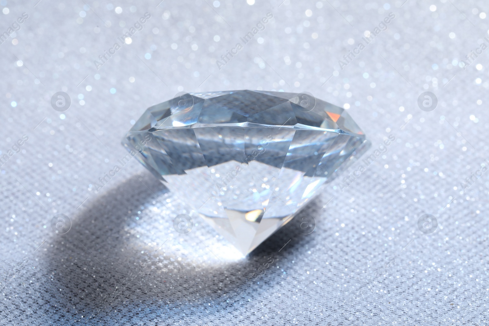 Photo of Beautiful dazzling diamond on white glitter fabric, above view