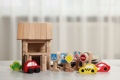 Set of wooden road signs, cars and house on light grey table indoors. Children's toys