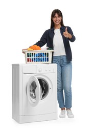 Photo of Beautiful woman with laundry basket showing thumbs up near washing machine on white background