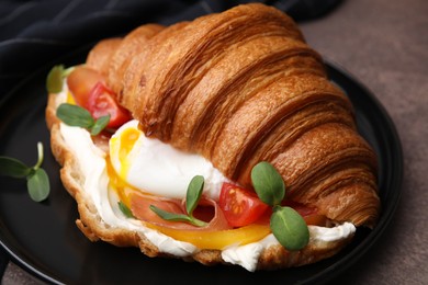 Tasty croissant with fried egg, tomato and microgreens on brown textured table, closeup