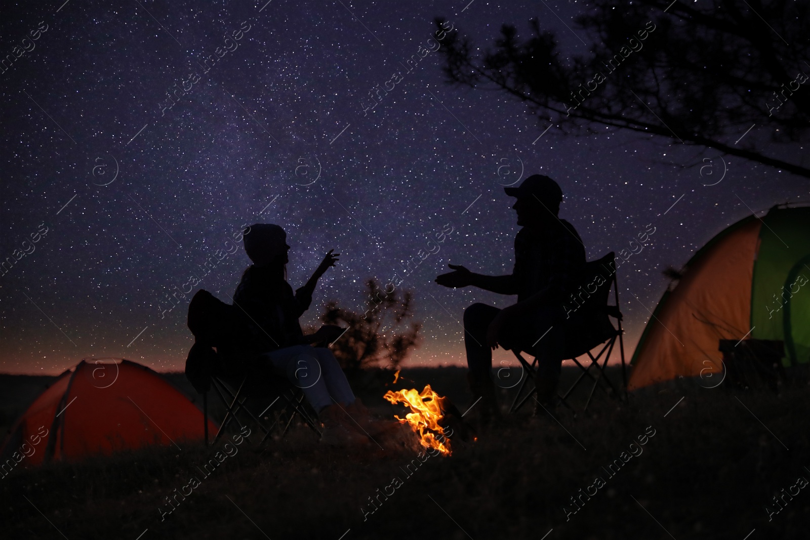 Photo of Silhouettes of couple near bonfire in evening. Camping season