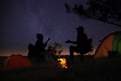 Photo of Silhouettes of couple near bonfire in evening. Camping season