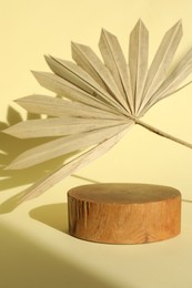 Photo of Presentation of product. Wooden podium and palm leaf on yellow background