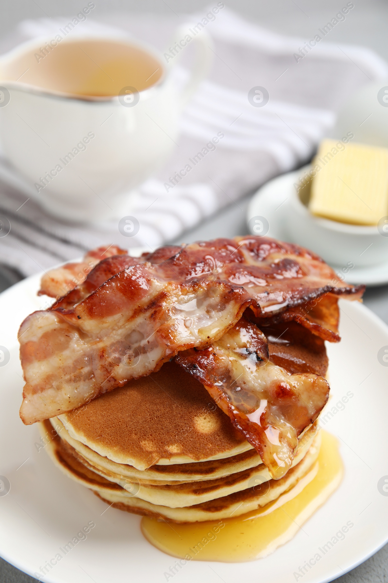 Photo of Delicious pancakes with maple syrup and fried bacon on plate, closeup