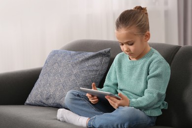 Photo of Little girl using tablet on sofa at home. Internet addiction