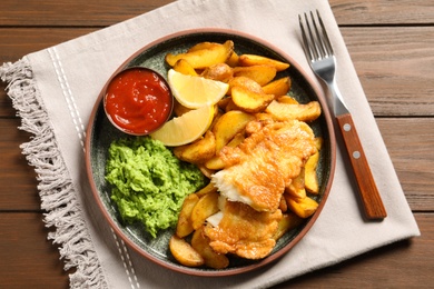 Plate with British traditional fish and potato chips on wooden background, top view