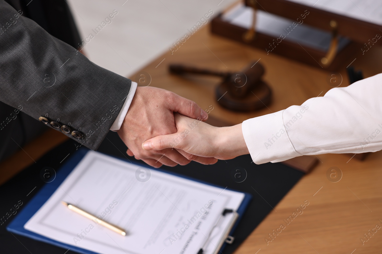 Photo of Notary shaking hands with client at wooden table in office, closeup