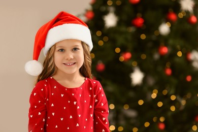 Photo of Portrait of cute happy girl wearing Santa hat at home, space for text. Christmas atmosphere